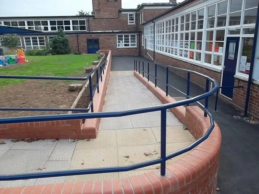 Paved access ramp with metal handrails outside a brick building