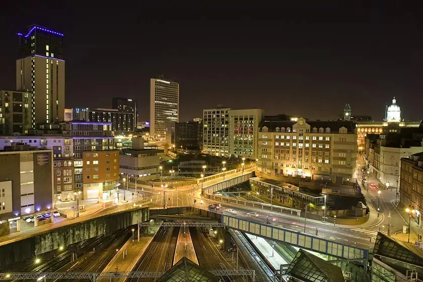 Illuminated city centre at night, with railway tracks in the foreground
