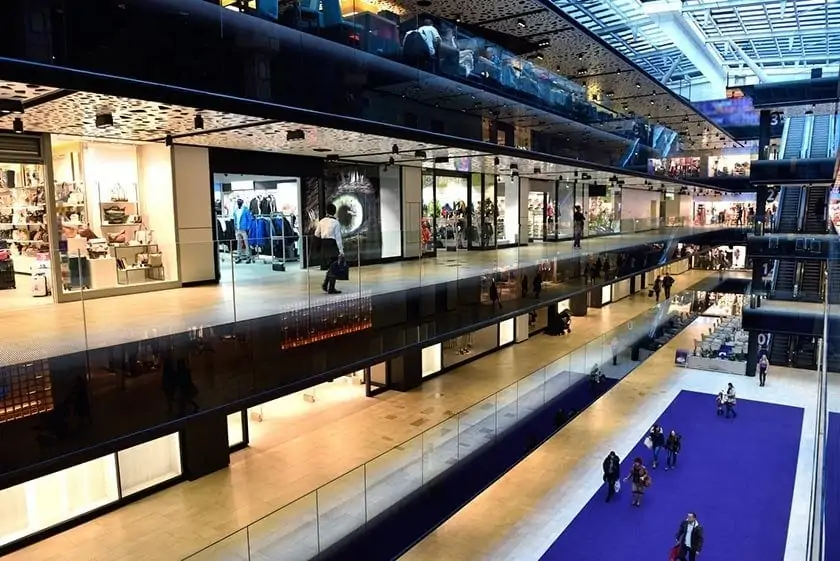 Interior of a modern shopping centre with illuminated shopfronts across two levels.