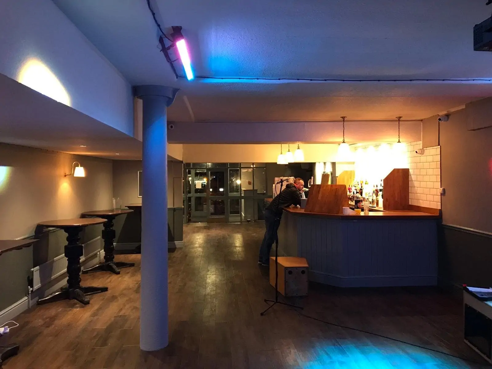 Dimly lit venue interior with a bar counter, wooden floor and a person leaning at the bar