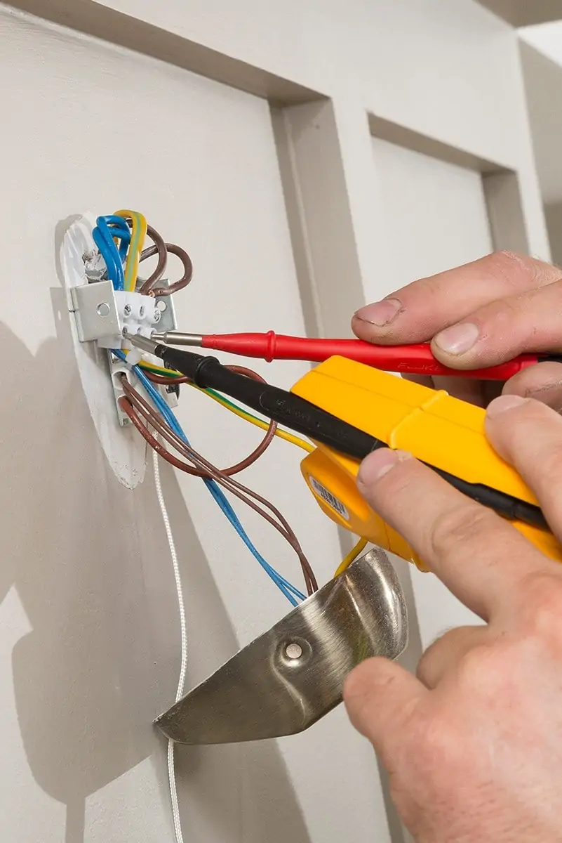 Hand using electrical testing tools on exposed wall wiring
