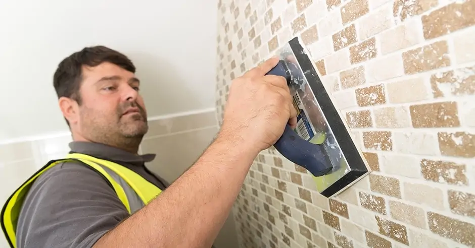 Worker in a high-visibility vest using a hand tool on a tiled wall