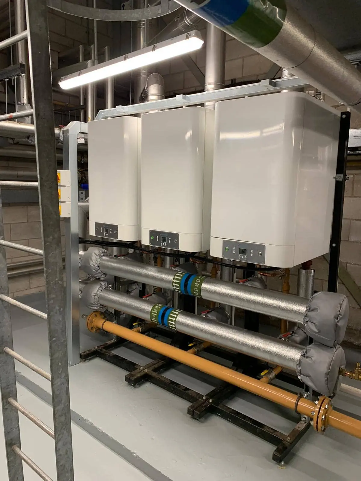 Three white heating units connected to pipework in a plant room