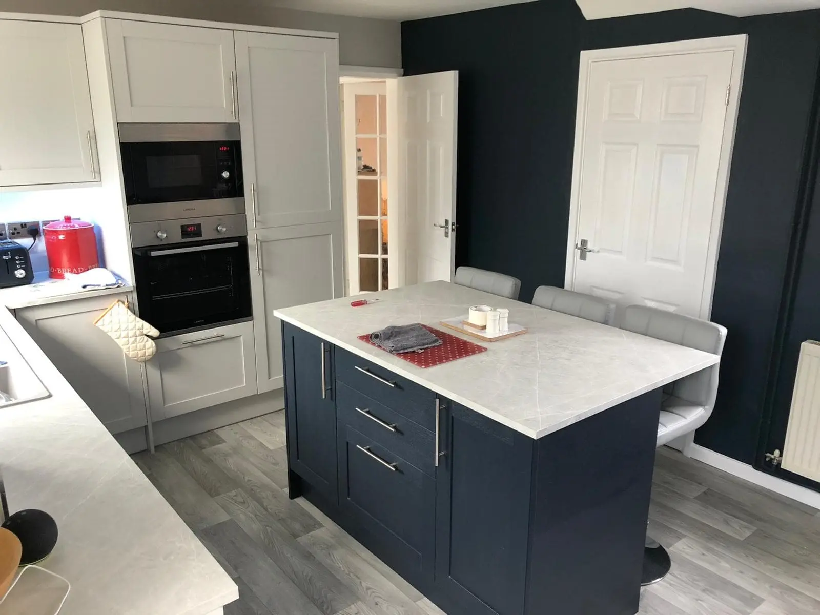 Reinstated kitchen with a dark blue island, white worktops and built-in appliances
