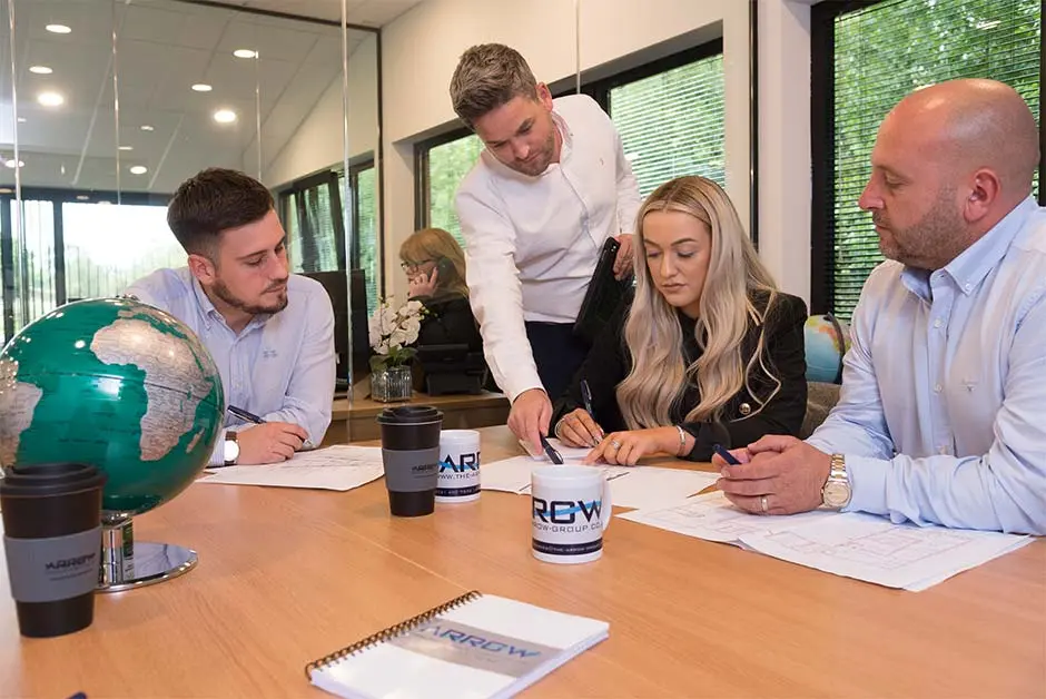 Four colleagues review documents around a table in an office meeting.
