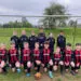 Youth football team in black and red kits posing in front of a goal with a football
